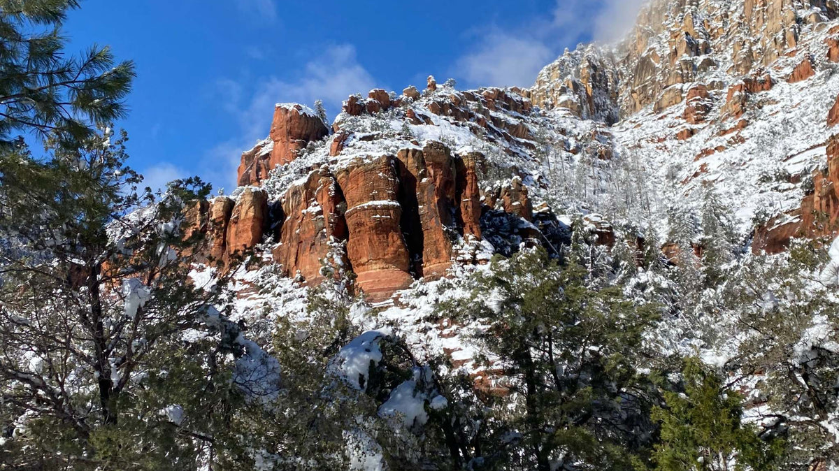Snow-covered red mountains and pine trees under a clear blue sky at the Sedona Mountain Bike Festival