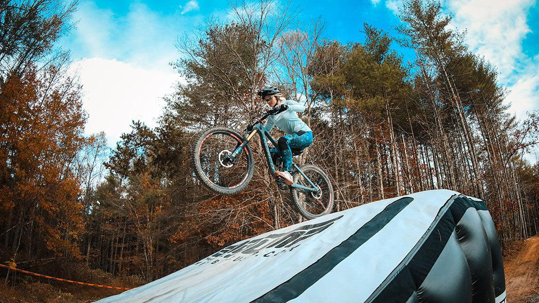 Mountain biker performing a jump at Kanuga Bike Park showcasing consistent training in an outdoor forest setting.