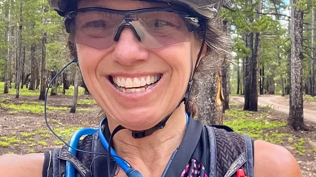 Smiling woman cyclist wearing helmet and sunglasses in forest during Leadville 101 MTB race training session
