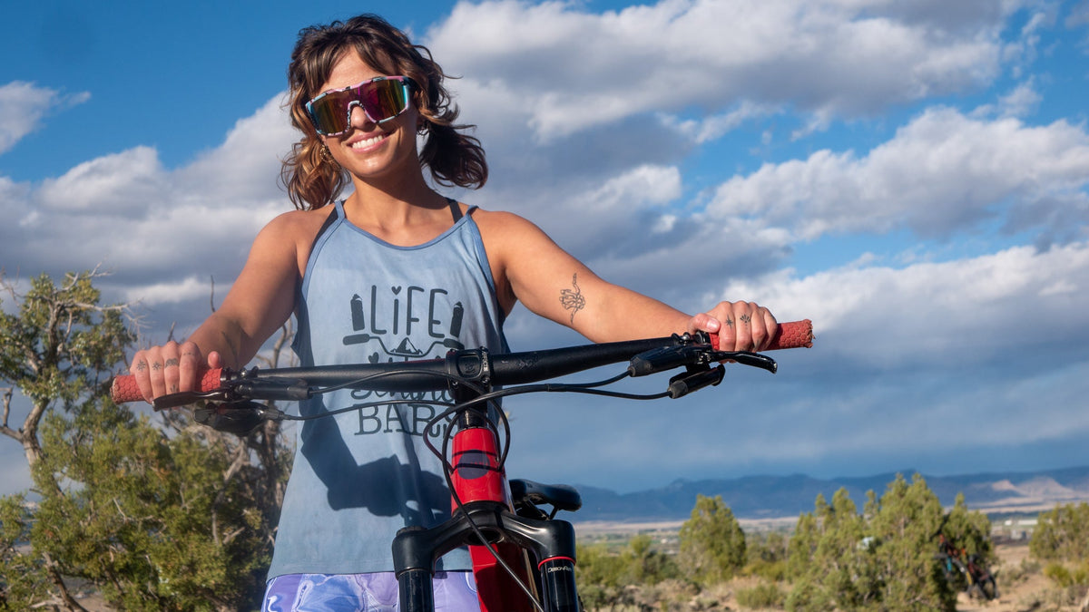 Cyclist wearing women's cycling shorts with 5" inseam, featuring comfort fit and moisture-wicking fabric, against scenic outdoor backdrop.