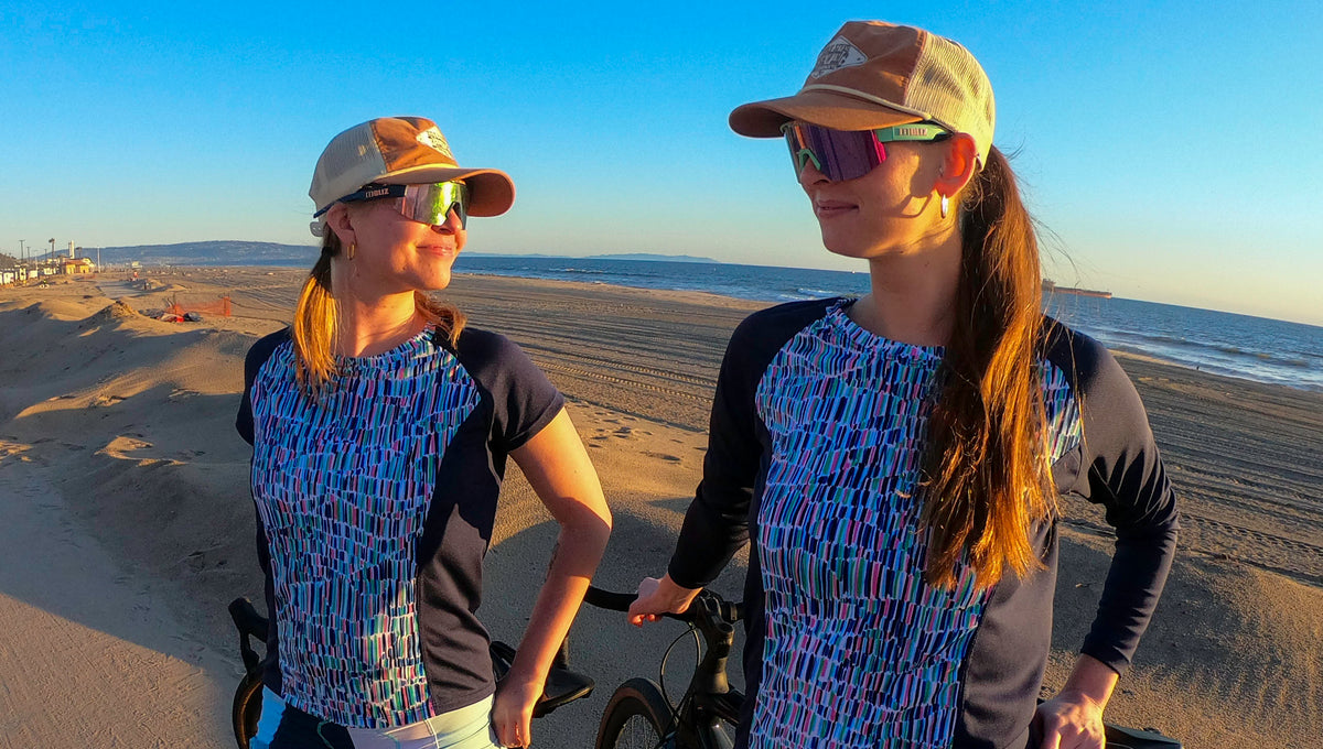 Moxie Tee Jersey Blues Long Sleeve worn by cyclists on a beach, showcasing performance fabric and moisture management technology.