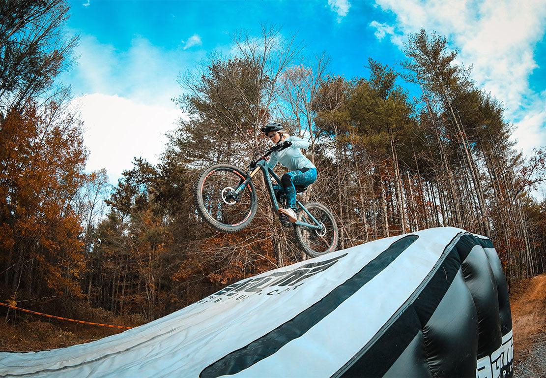Mountain biker performing a jump at Kanuga Bike Park showcasing consistent training in an outdoor forest setting.