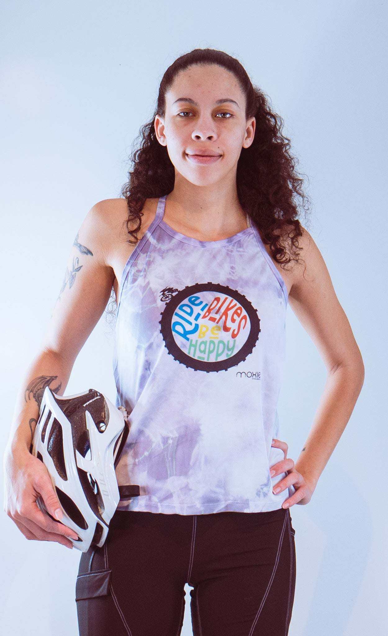 Woman wearing a purple tie-dye sleeveless cycling jersey holding a white bike helmet