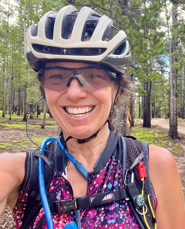 Smiling woman cyclist wearing helmet and sunglasses in forest during Leadville 101 MTB race training session