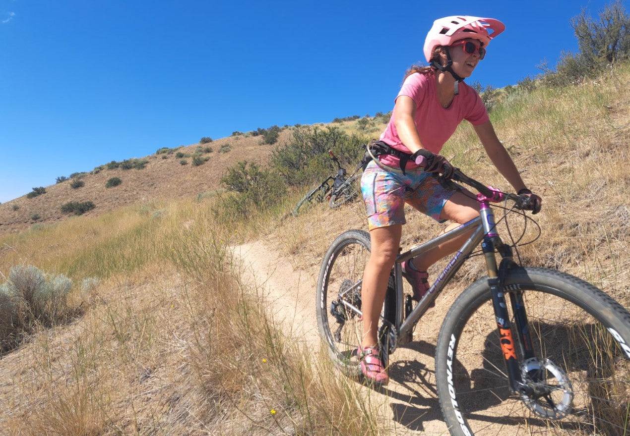 Woman mountain biking on trail wearing pink helmet and colorful cycling shorts during Femme Cyclist Review