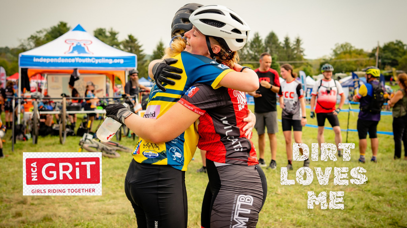 Two female cyclists in helmets hugging at an outdoor youth cycling event promoting Support PICL with NICA GRiT and "Dirt Loves Me" text.