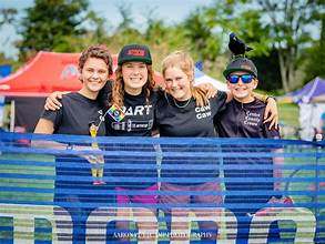 Four smiling young cyclists standing behind a blue barrier, supporting the Support PICL initiative and promoting inclusivity in youth cycling.