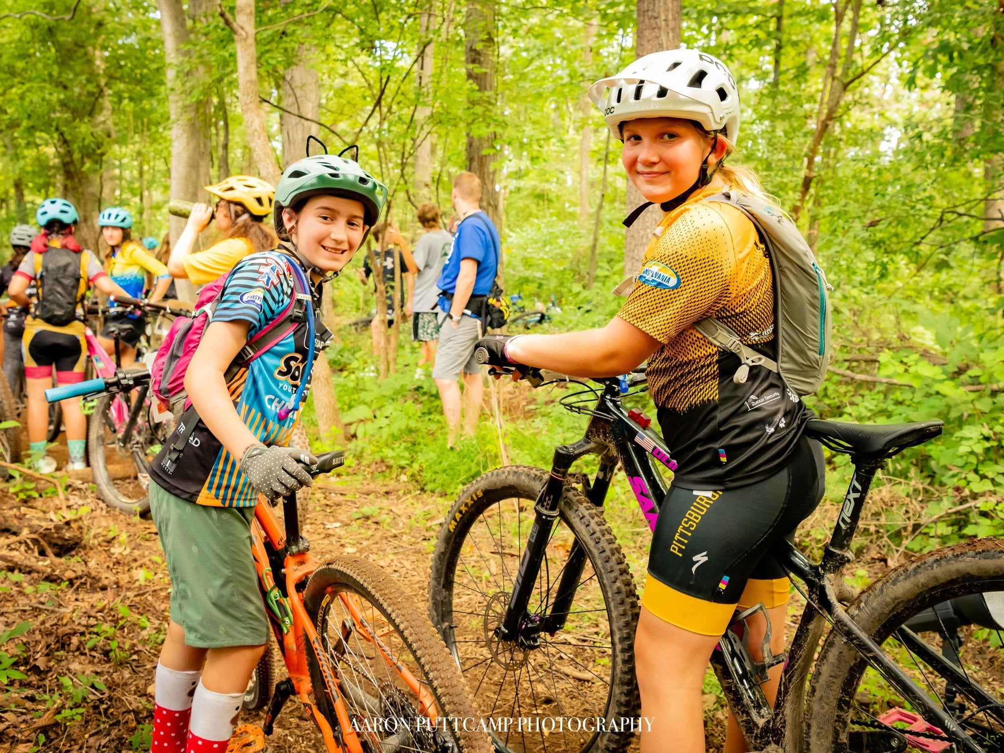 Children smiling with mountain bikes in a forest trail promoting Support PICL and youth cycling inclusivity