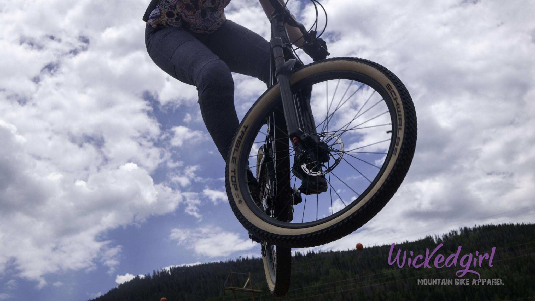 Bike rider wearing Smoke Denim cycling pants mid-jump against a cloudy sky.