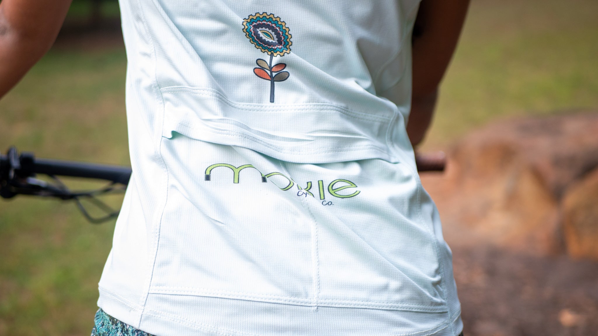 Women wearing Moxie Tee Cycling Jersey with Tree of Life graphic on bike trail back view