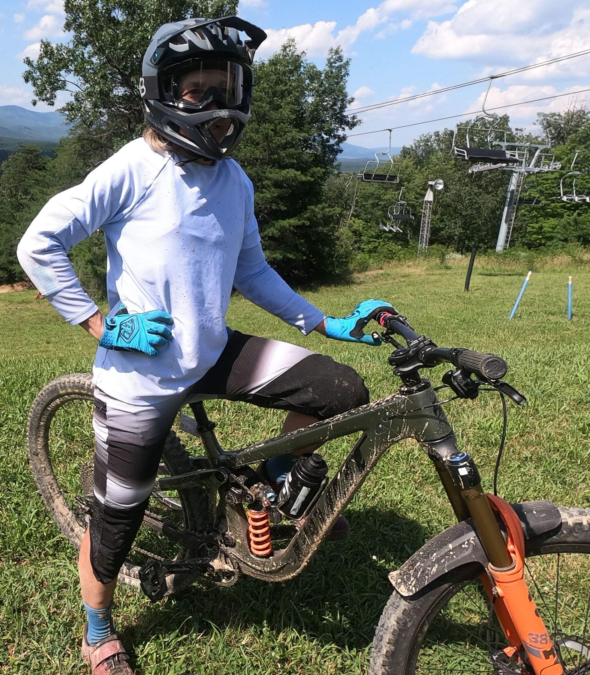 Mountain biker wearing black and white stripe bike pants with removable G-Form knee pads standing next to a muddy bike on grassy trail