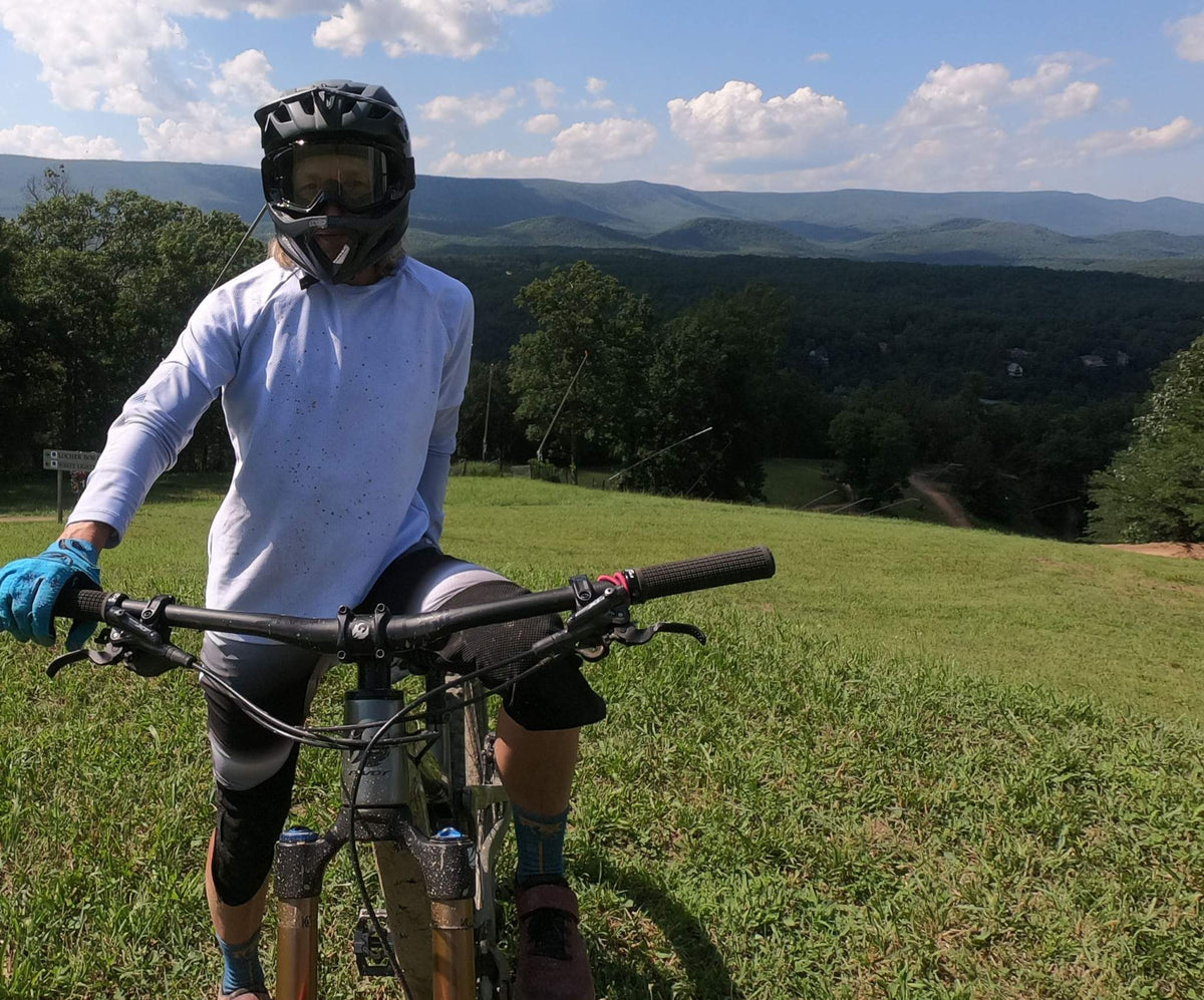 cyclist wearing black and white stripe bike pants with removable G-Form knee pads riding mountain bike on grassy hill with scenic mountain background