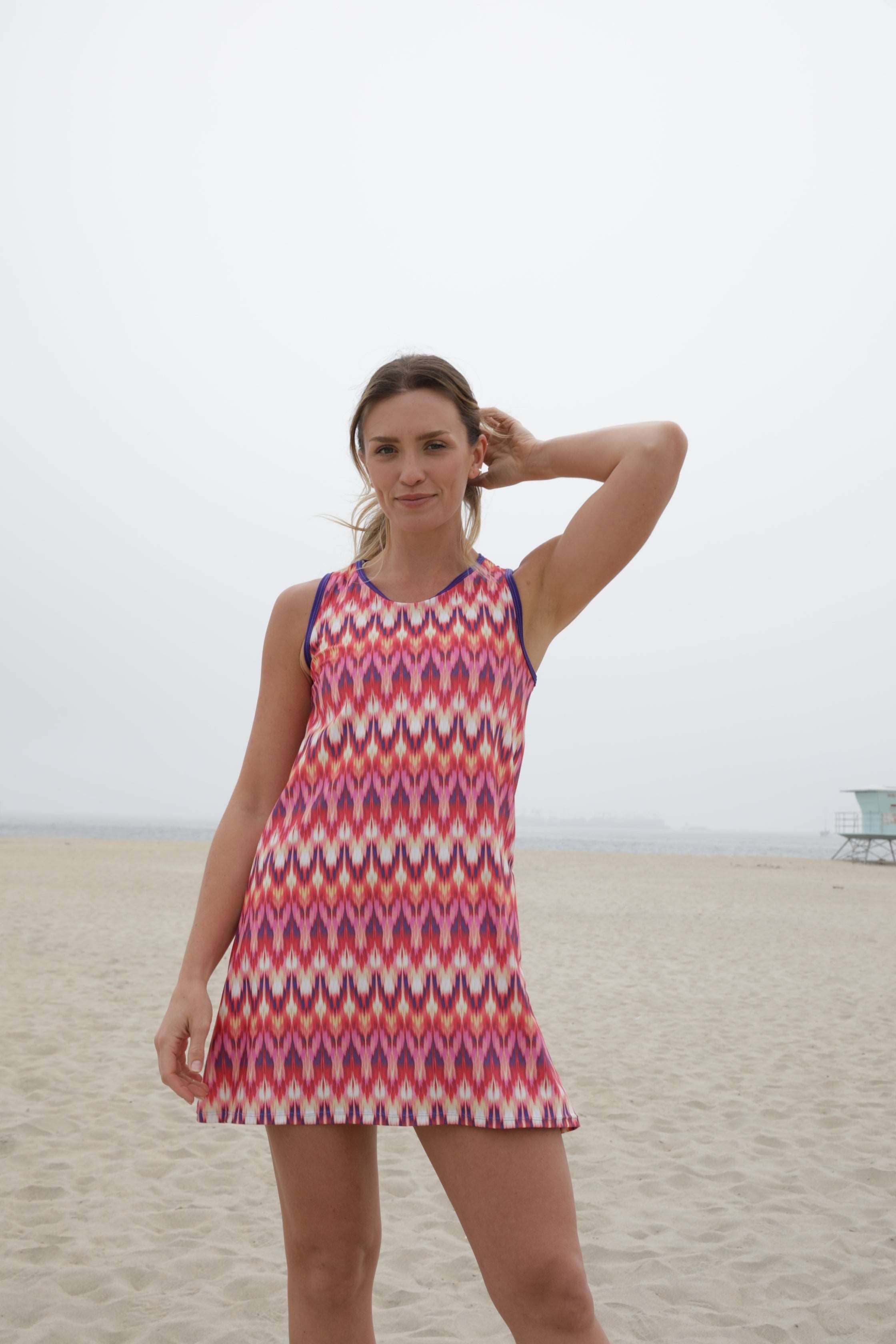 Sporty pink patterned Mod sports dress with scoop neckline and A-line cut on a beach.