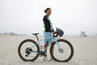Moxie Hoodie High Visibility Color Wave worn by cyclist on a beach with bike.