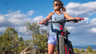 Woman wearing cycling shorts with 5" inseam and riding a bike in a scenic outdoor setting.