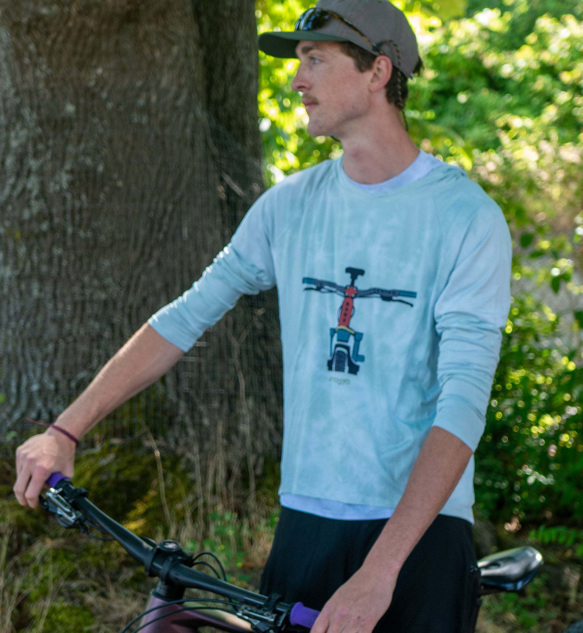 A man wearing a light green hoodie jersey by Moxie Cycling  riding a mountain bike