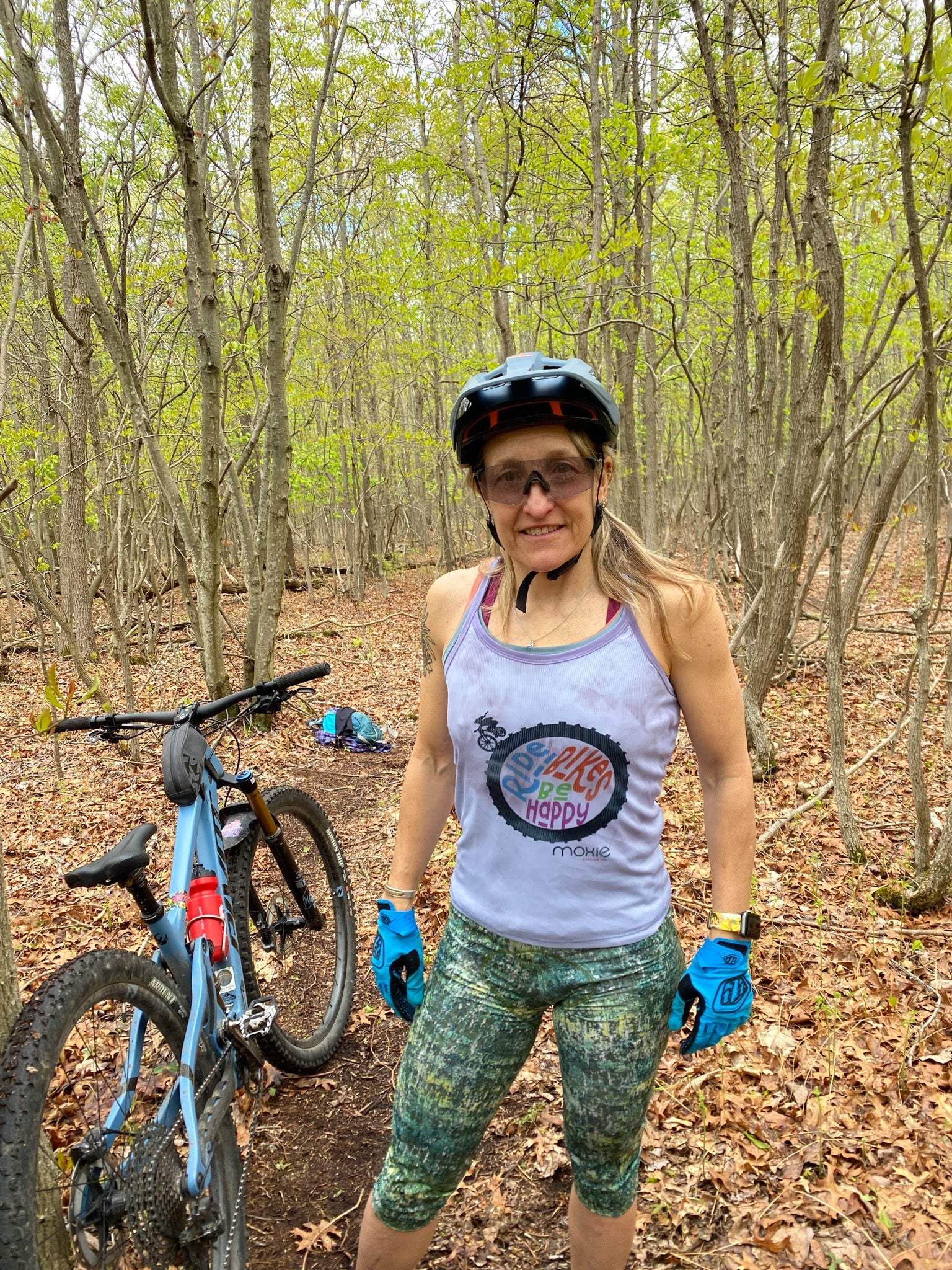 Woman wearing green cycling knickers standing next to a mountain bike in a forest.