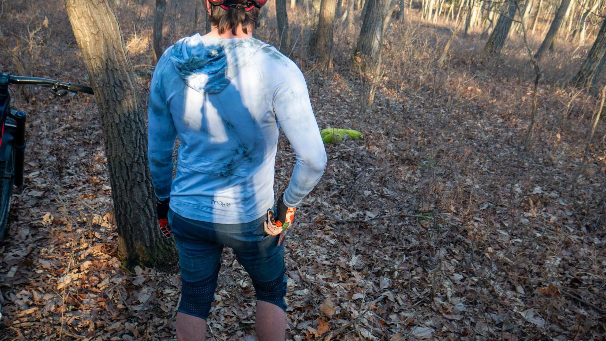 All Gender Hoodie with high-visibility fabric and back pockets worn by cyclist in forest.
