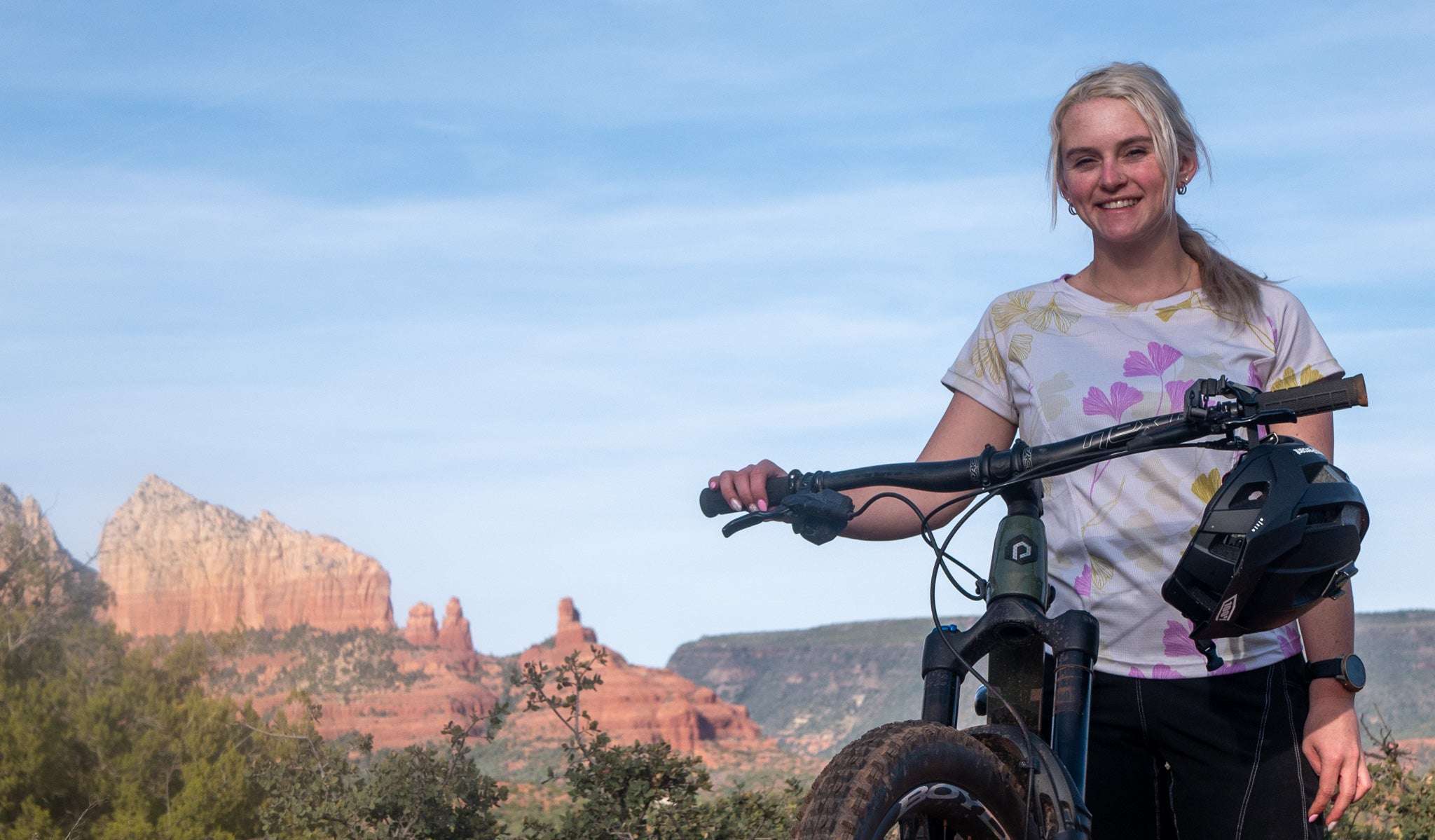 Woman wearing Moxie Tee Jersey Moss Floral standing with mountain bike in outdoor desert landscape