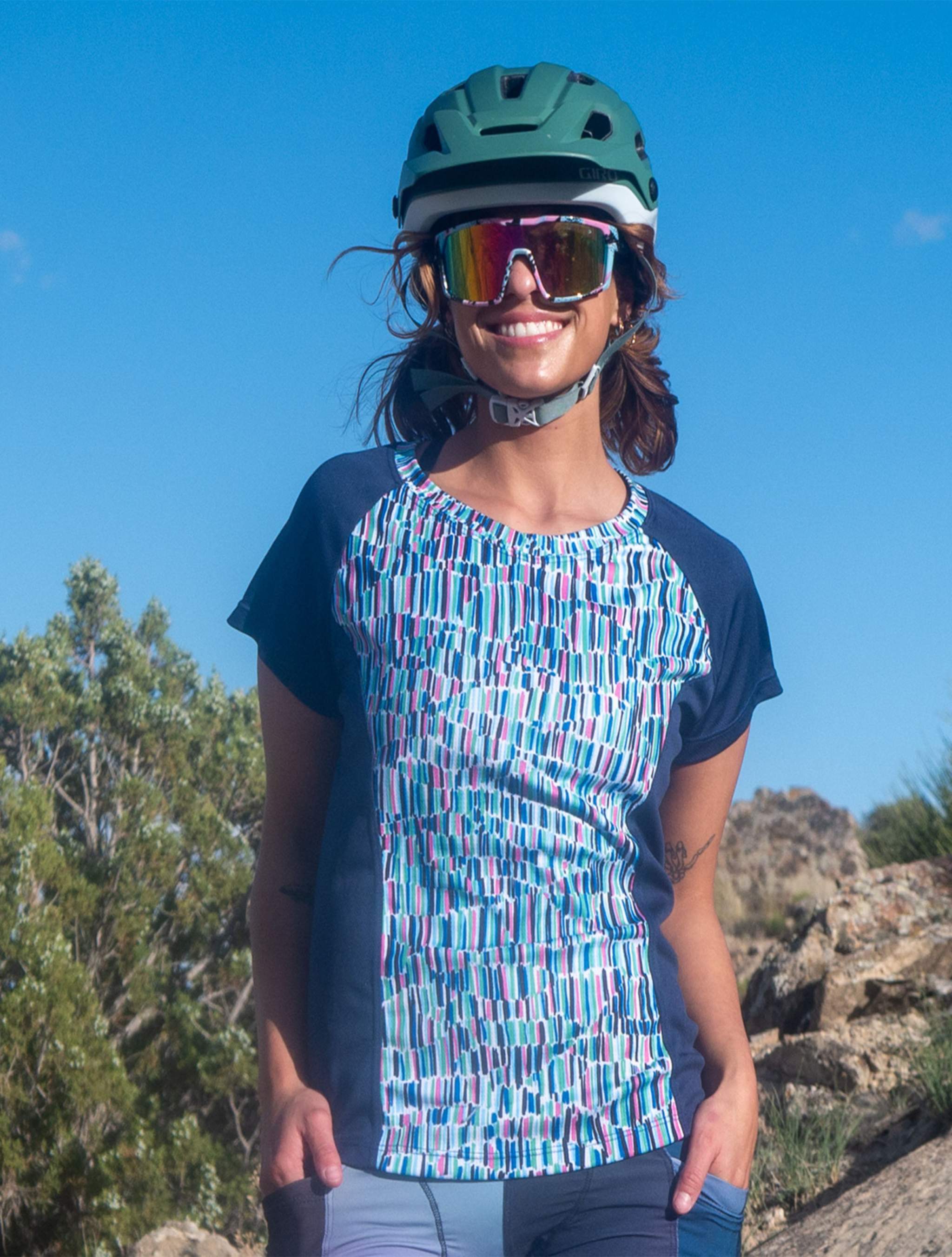 Woman wearing Moxie Tee Jersey with colorful pattern and navy sleeves outdoors on a sunny bike ride