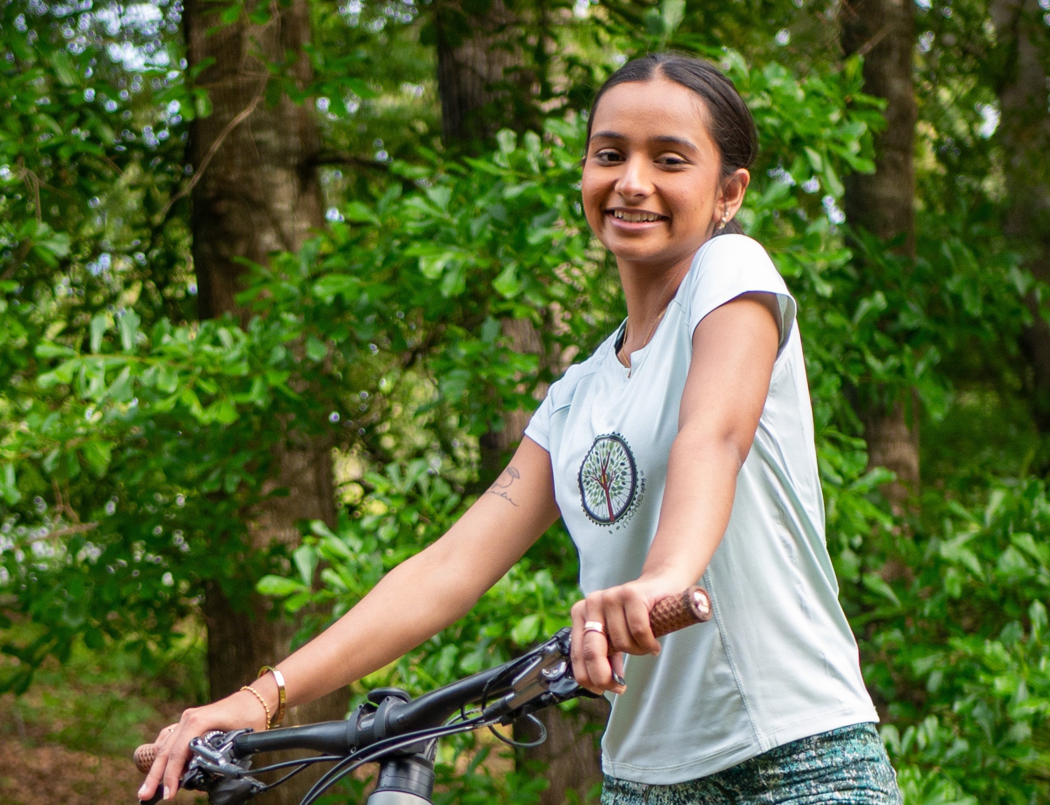 Women wearing Moxie Tee Cycling Jersey with Tree of Life graphic on bike trail