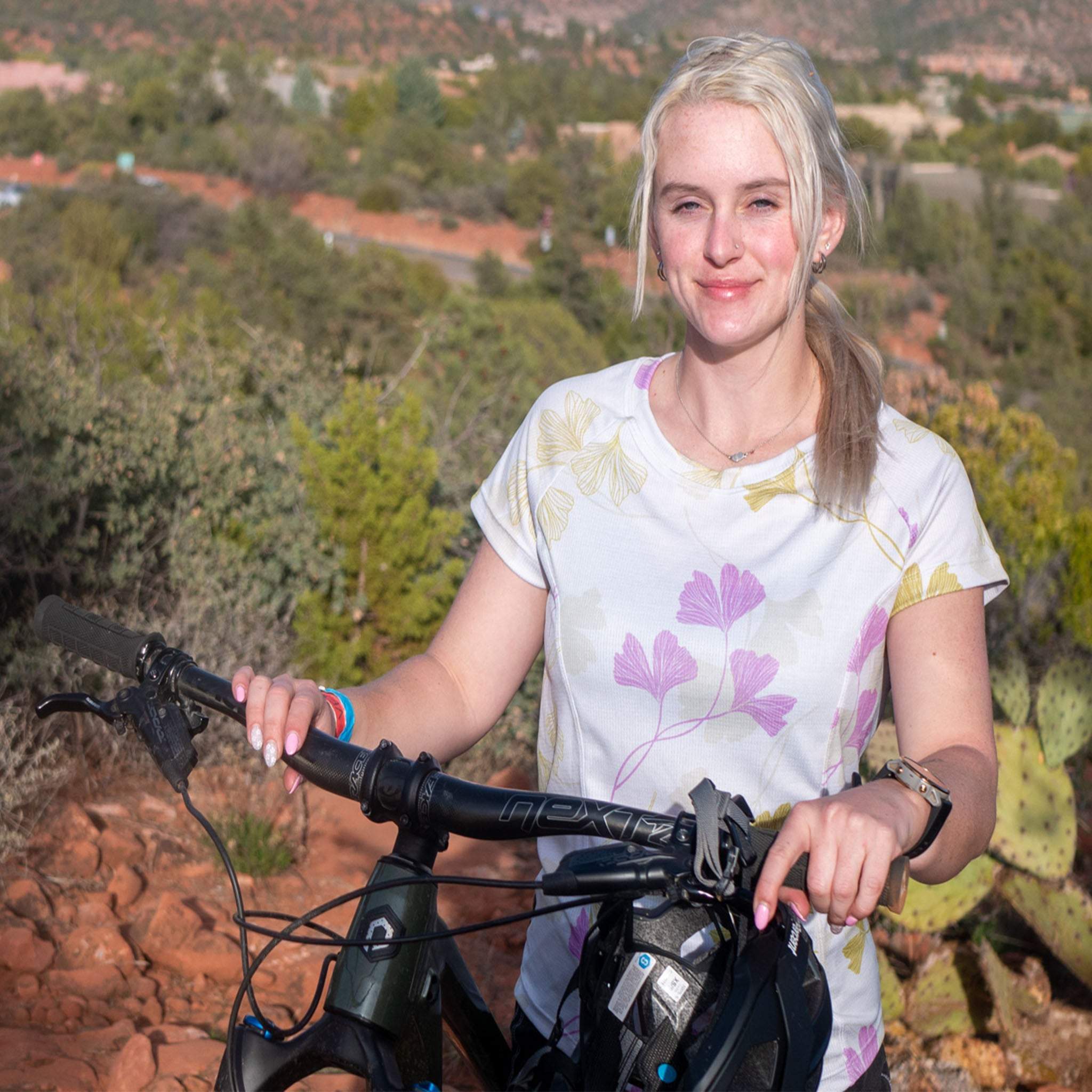 Woman wearing Moxie Tee Jersey Moss Floral floral print bike jersey outdoors with bicycle.