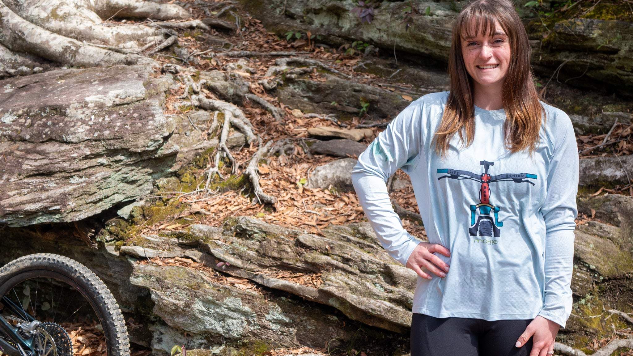 Person wearing a light green mountain bike hoodie with a graphic design in a forest setting