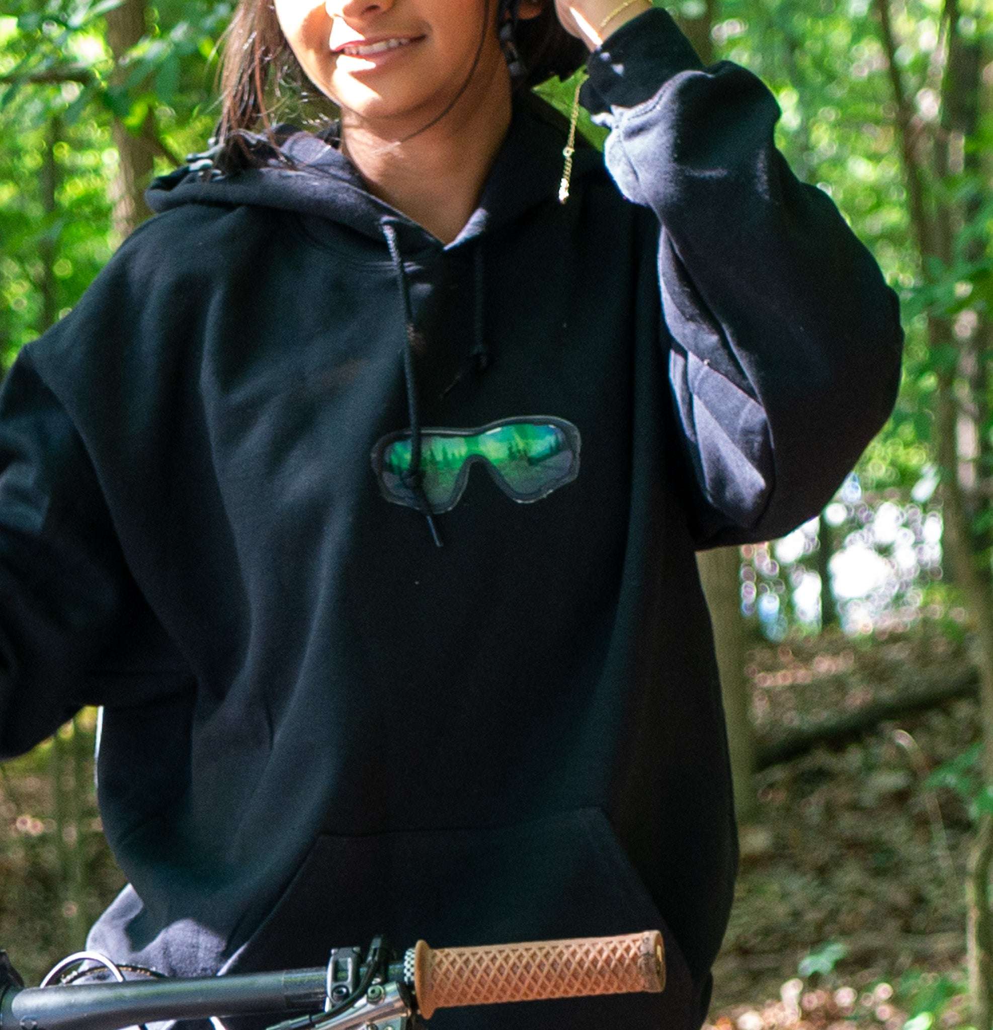 Person wearing a black hoodie with sunglasses design in a forest setting