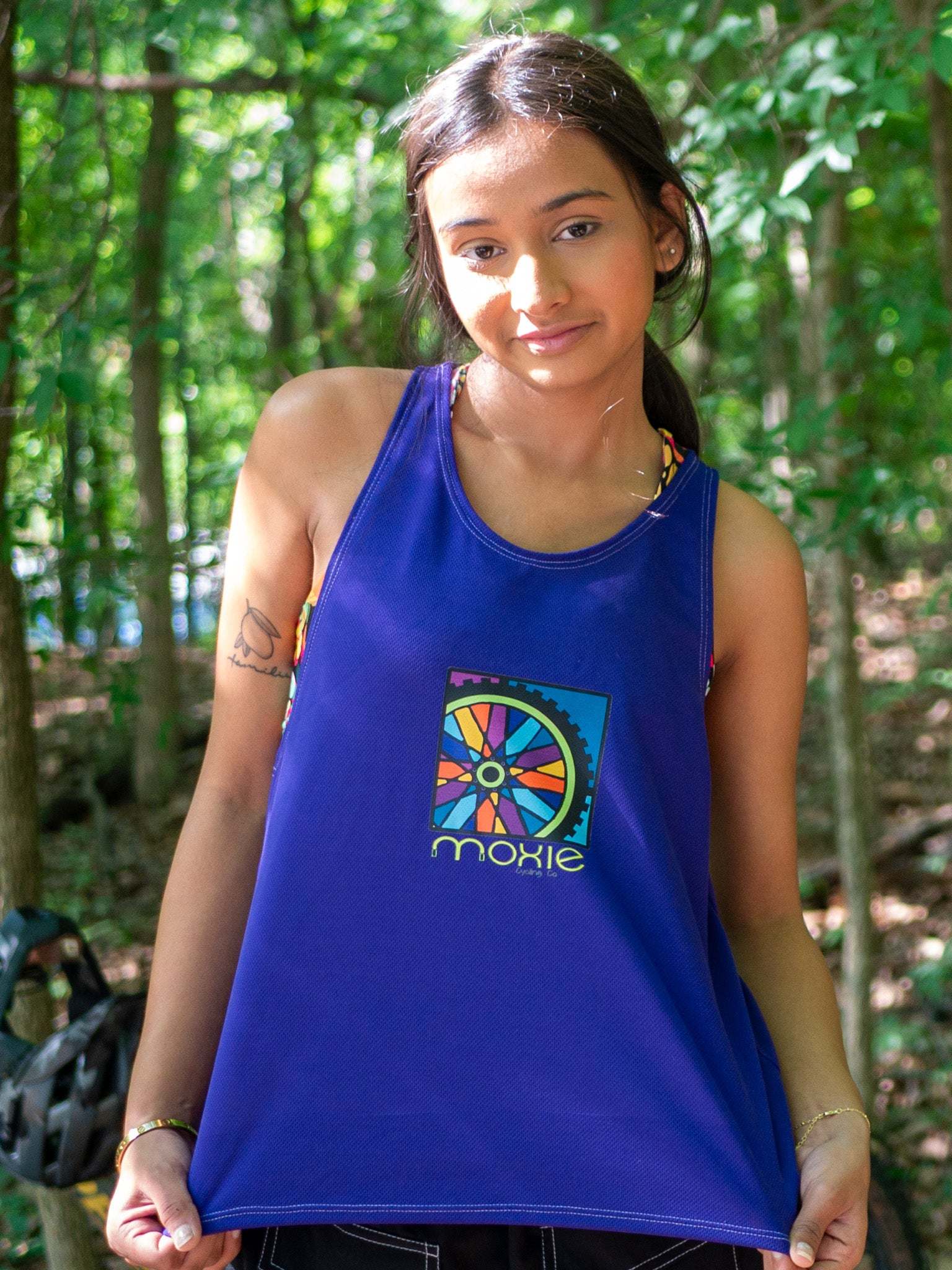 Women wearing Moxie Tech Tank breathable mesh cycling jersey with Ride Bikes Be Happy graphic on mountain trail