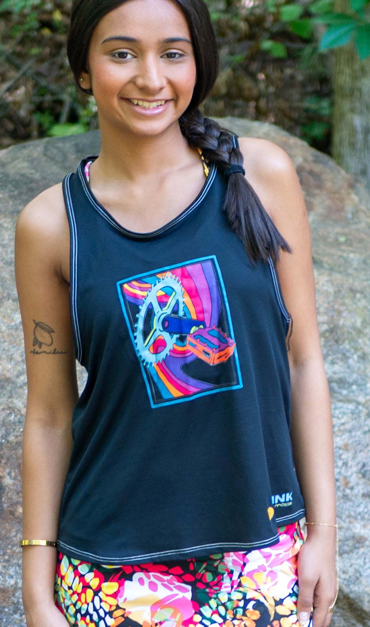 Woman wearing Moxie Tech Tank breathable mesh cycling jersey with Ride Bikes Be Happy graphic on a mountain bike trail