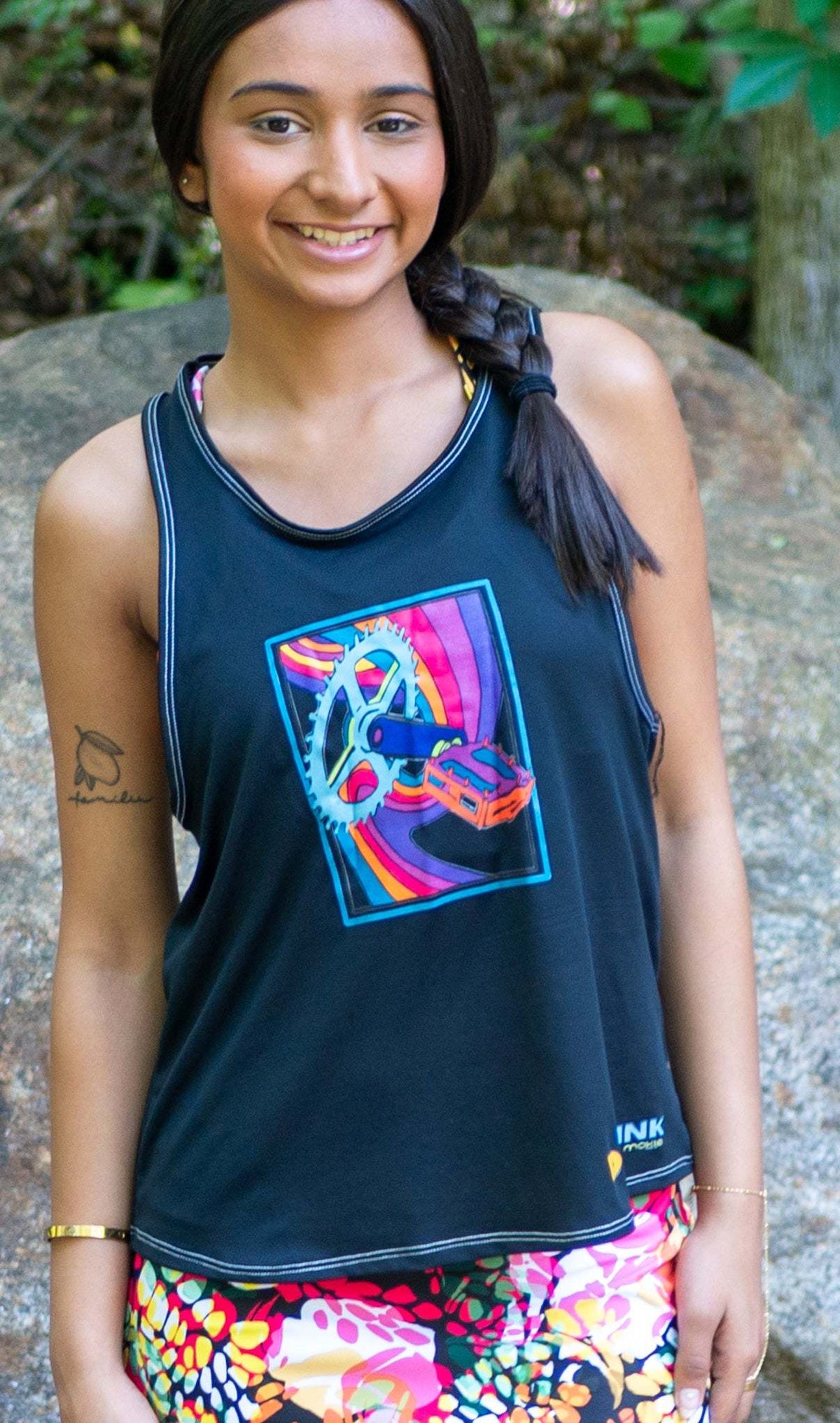 Woman wearing Moxie Tech Tank breathable mesh cycling jersey with Ride Bikes Be Happy graphic on a mountain bike trail