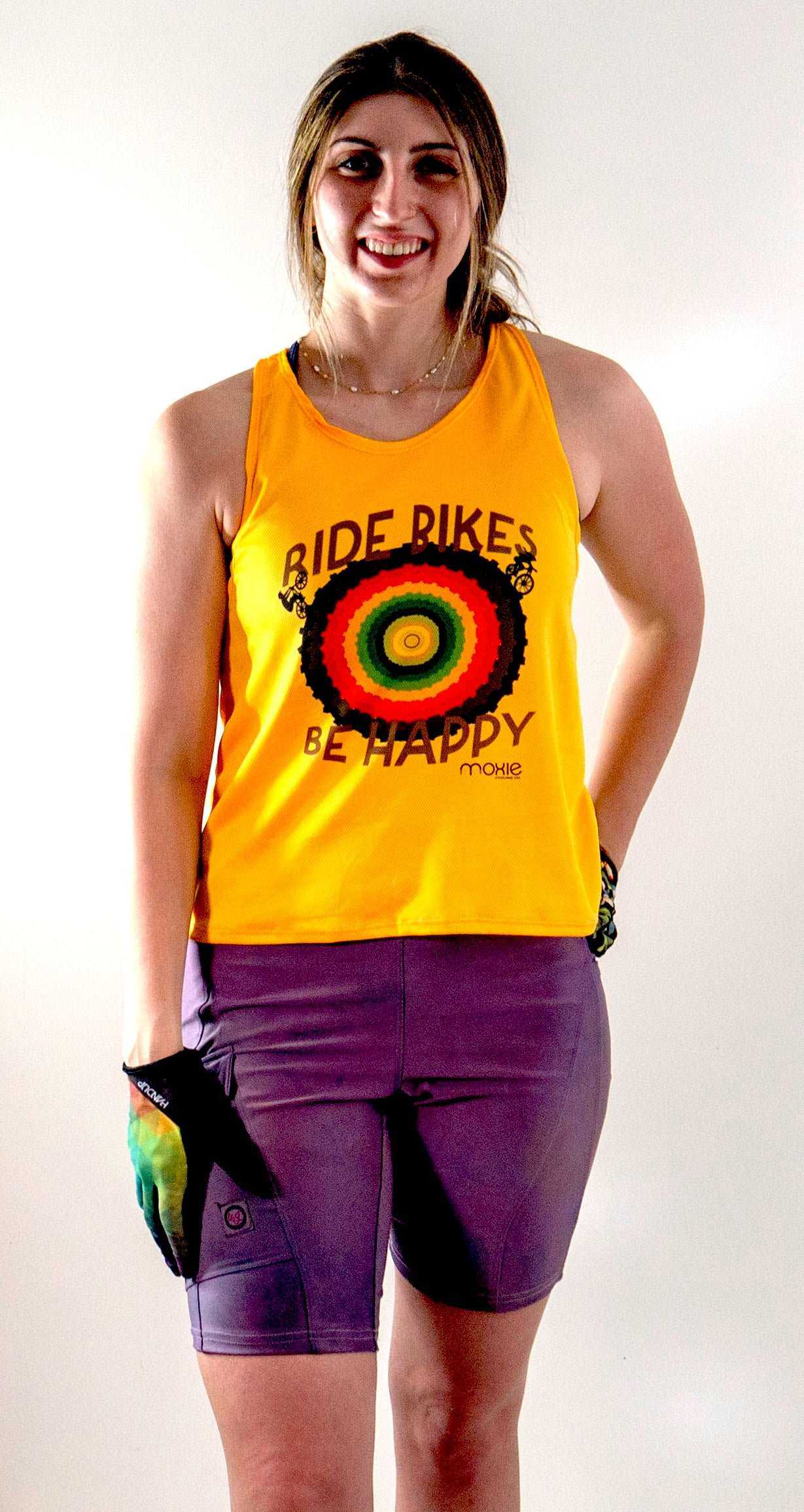 Woman wearing the 'Ride Bikes Be Happy Tank Pride', a vibrant yellow tank top with rainbow design, made of breathable light mesh fabric with moisture-wicking properties.