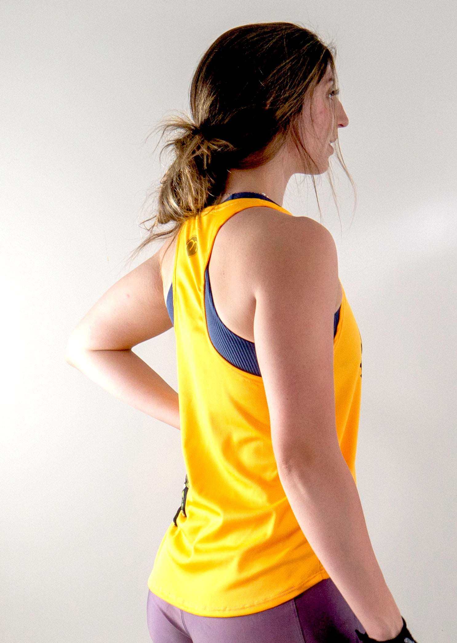 Woman wearing a yellow "Ride Bikes Be Happy" tank top with breathable mesh fabric and moisture-wicking design.