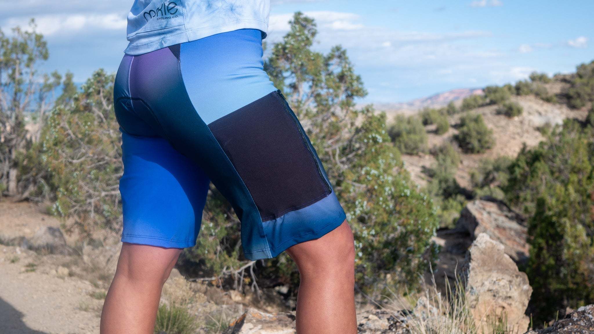 Steezy Stretch Bike Shorts Blues with side pocket, mountain scenery background.