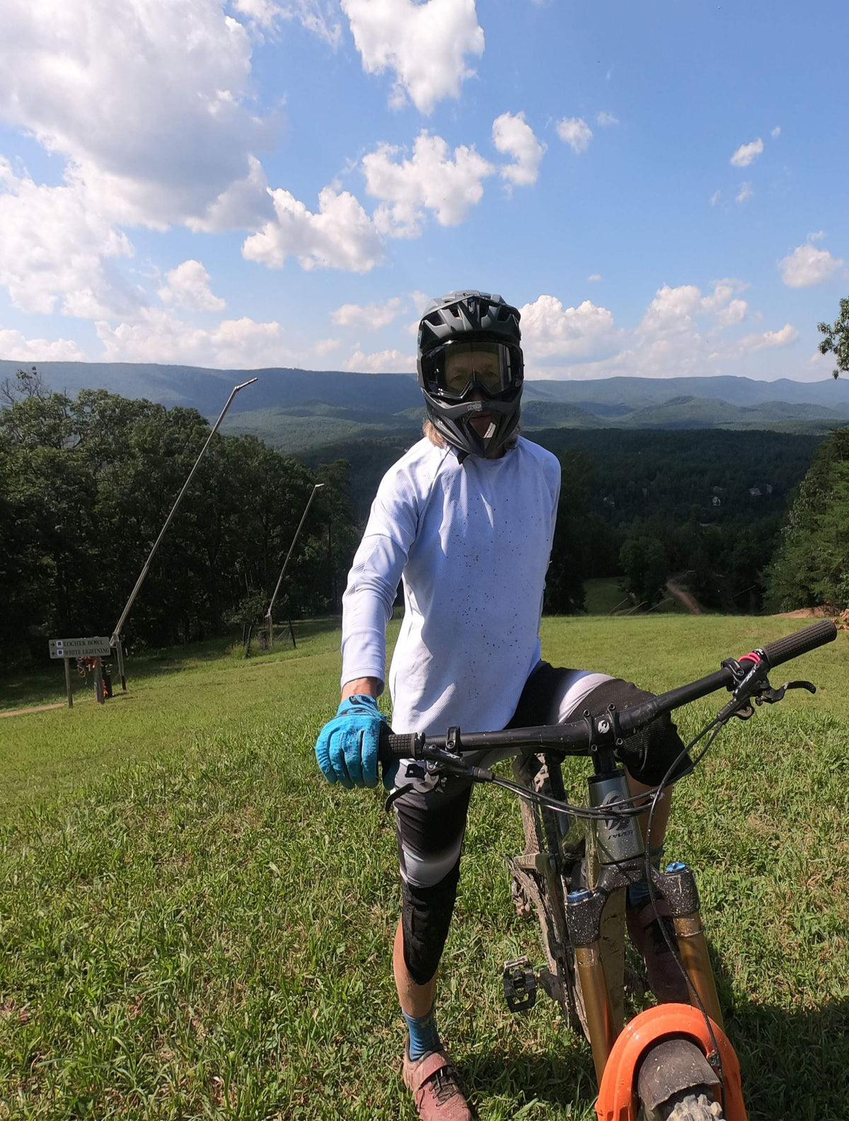 Woman wearing women's mountain bike pants with removable G-Form hip and knee pads standing with mountain bike on grassy hill under blue sky