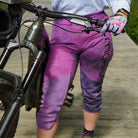 Purple electric bloom bike pants with removable G-Form knee pads worn by cyclist on bike trail