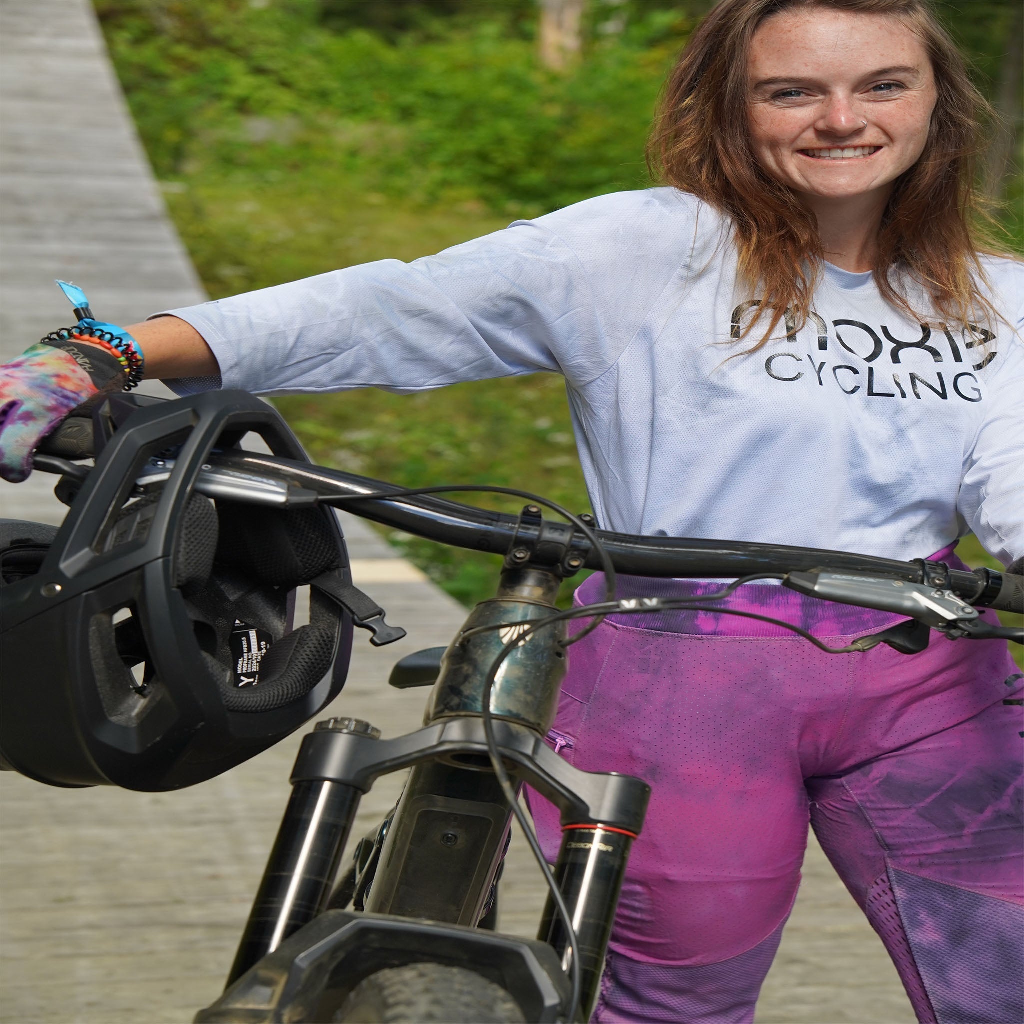 Woman wearing Electric Bloom bike pants with removable G-Form knee pads holding a mountain bike and helmet outdoors