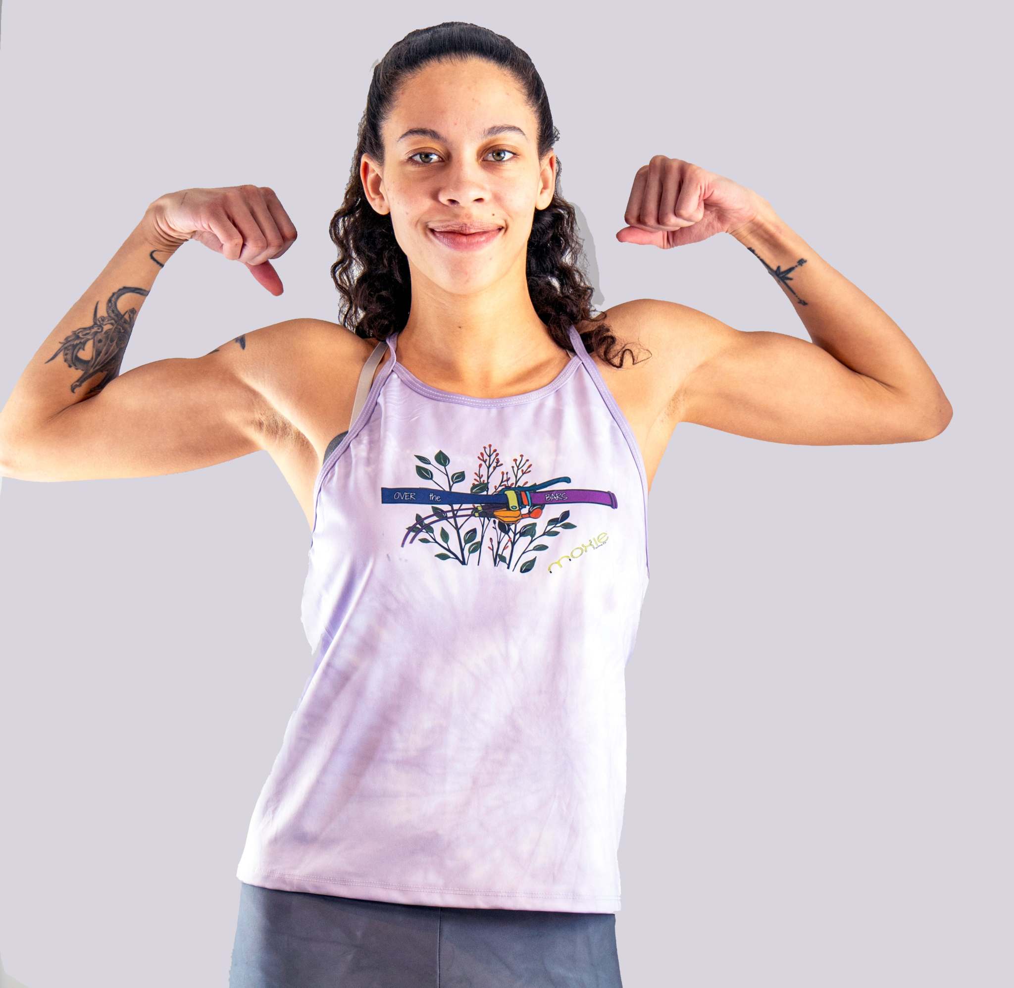 Woman flexing her muscles wearing a light purple sleeveless jersey with Over the Bars graphic