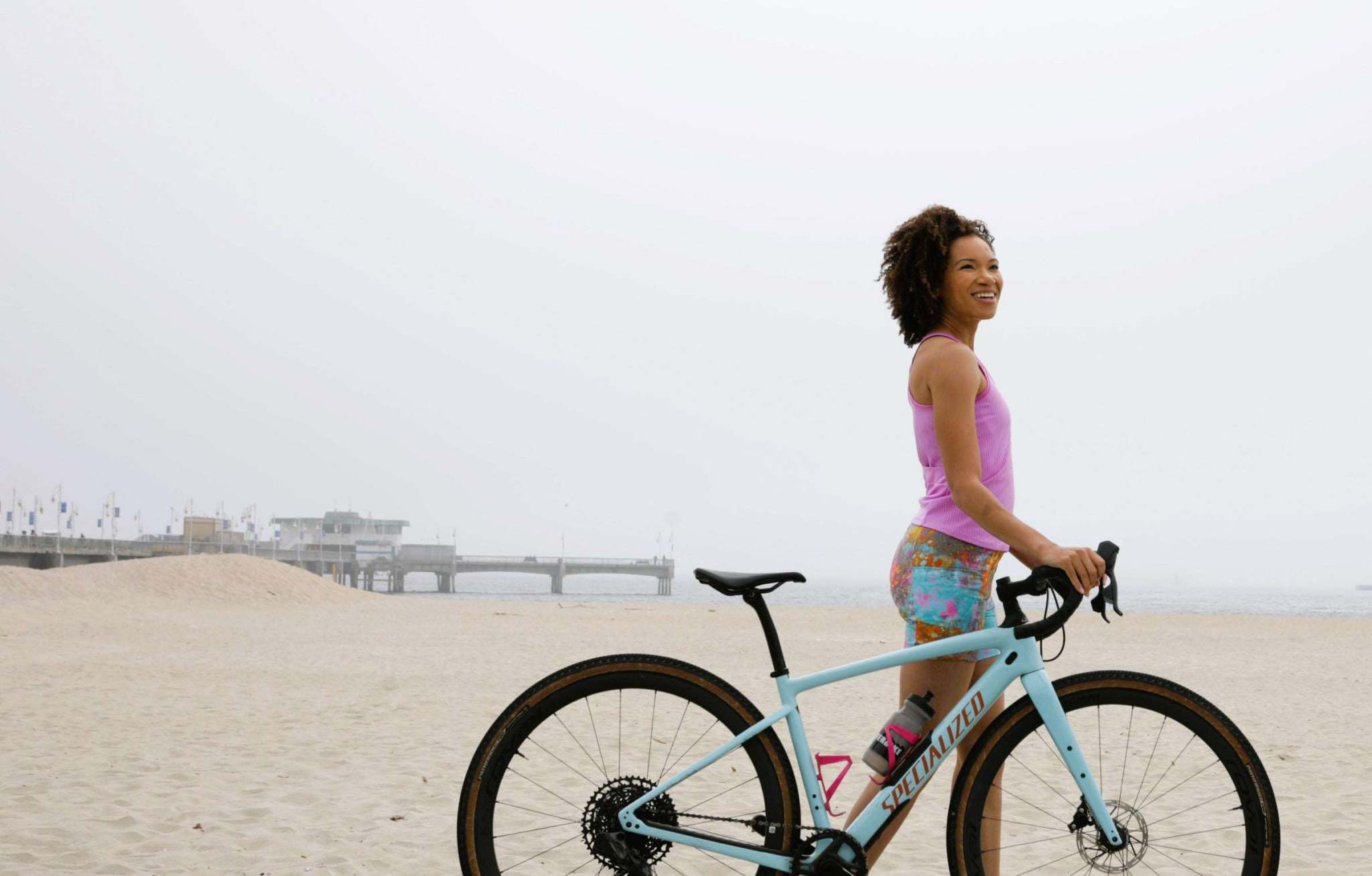 Woman wearing Lead Out Cycling Shorts Wild Fire with bicycle on the beach.